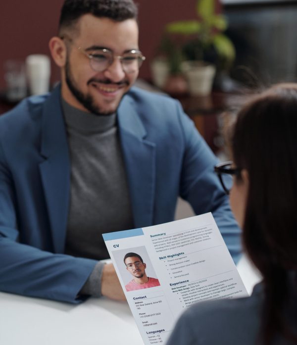 Vertical over shoulder view of young HR manager reading CV with smiling candidate sitting across table